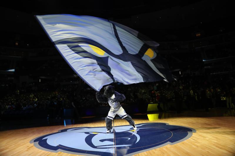 Grizzlies mascot Grizz (a bear) stands in the middle of the court over the Grizzlies logo while waving a grizzlies logo flag