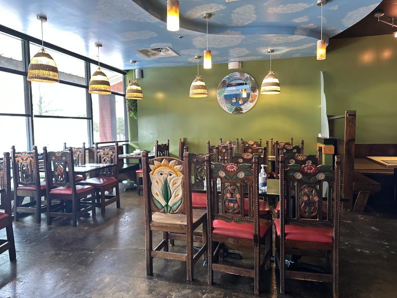 interior dining room of JJ's Tropical. Multiple six person tables, green back wall, and cloud painted ceiling
