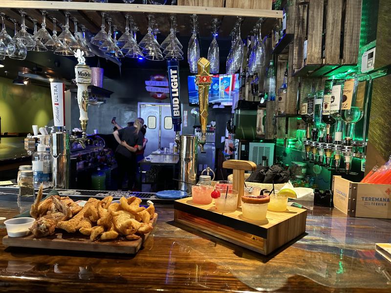 wings and catfish plate sitting on bar next to flight of margaritas