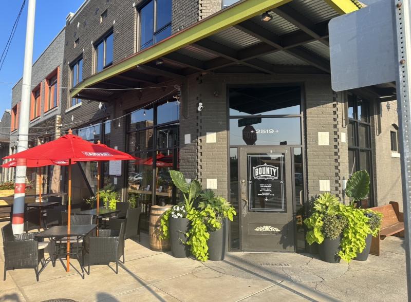 exterior entrance to bounty on broad green awning with patio seating to the side