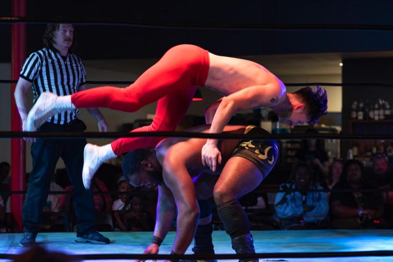wrestler flies over the back of another wrestler who is bent over