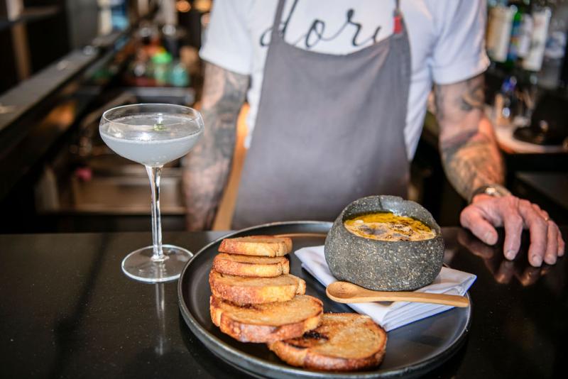 man stands behind bar with appetizer and mocktail sitting on bar