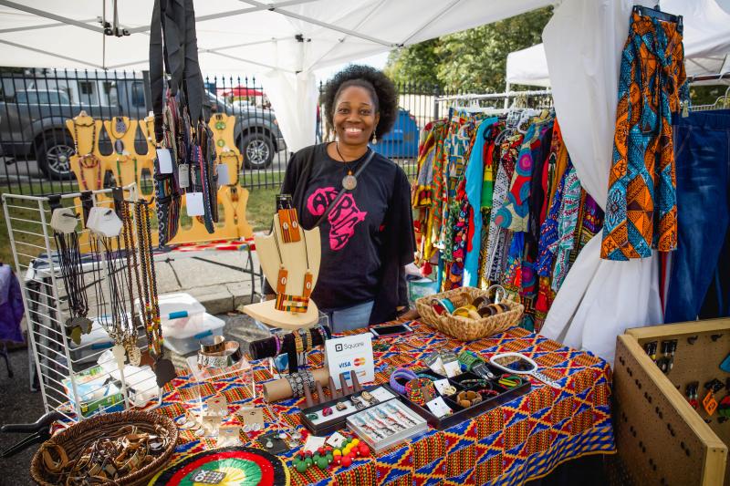 woman poses behind table of her vendor shop of jewelry and clothes