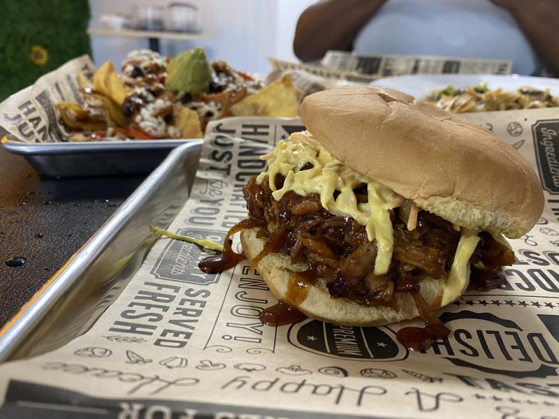 pulled pork sandwich on tray with bbq fajita nachos in background