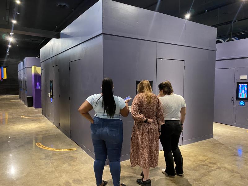 three women stand outside the warehouse game pod