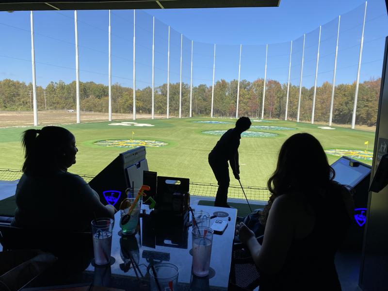 people sitting at bar table watching guy play topgolf