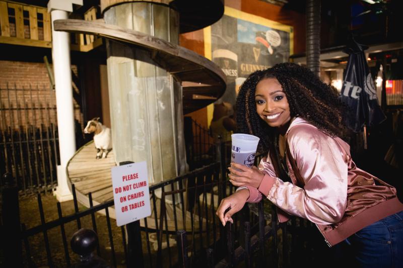 woman poses with beer in front of goat pin