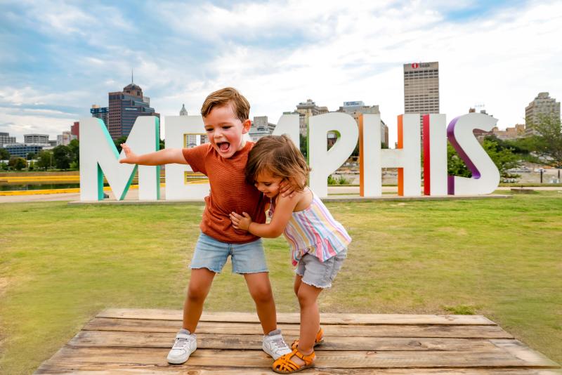 two children pose in front of large Memphis letters sign