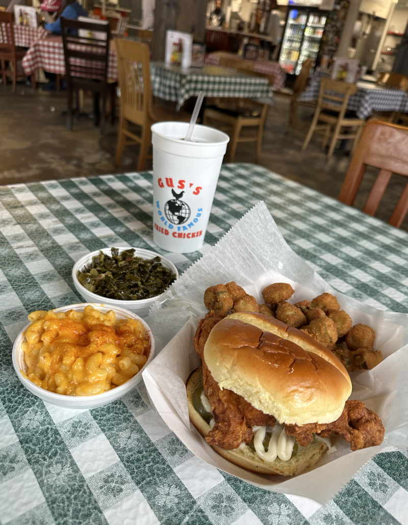 chicken sandwich, fried okra, Mac and cheese, collard greens on a plate on top of green and white striped table cloth