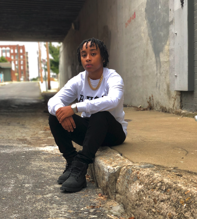 artist Jus Bentley sits on curb for a photo