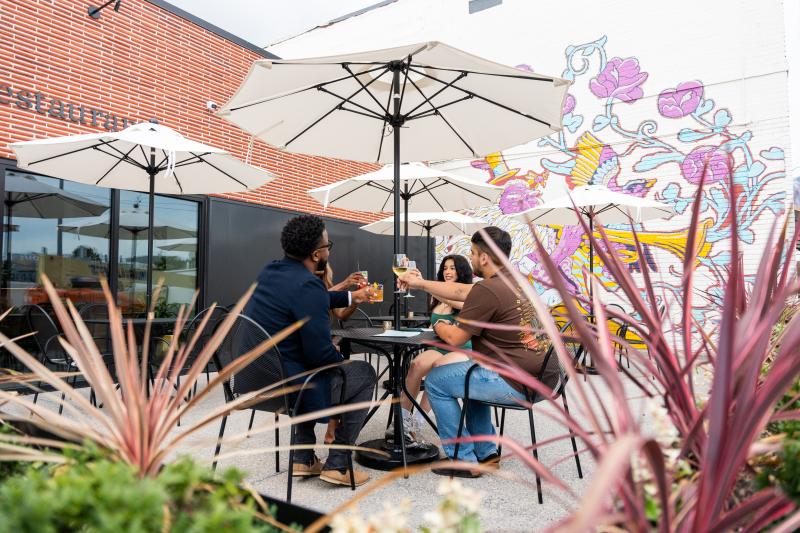 four friends sitting on outdoor patio toasting drink