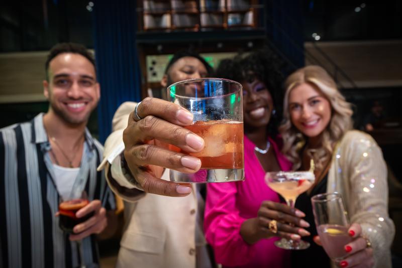 four friends hold up cocktails and smile for photo