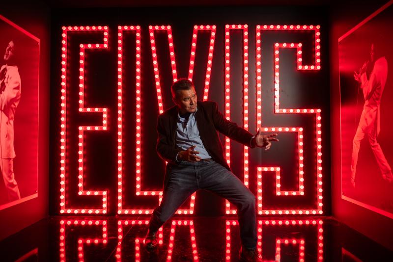 man poses in front of big elvis letters