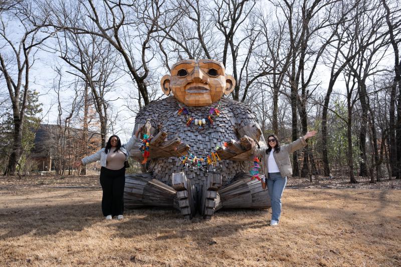two women pose for photo next to giant troll on display