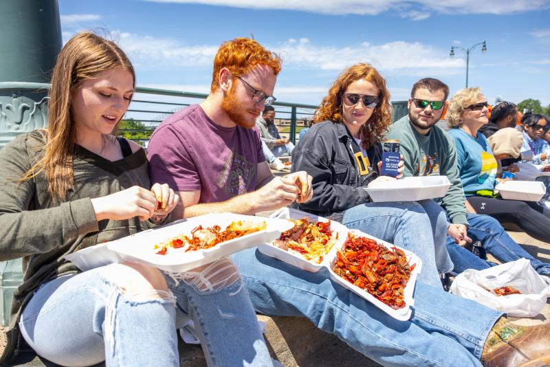 a group of four people sitting on curb eating crawfish out of containers