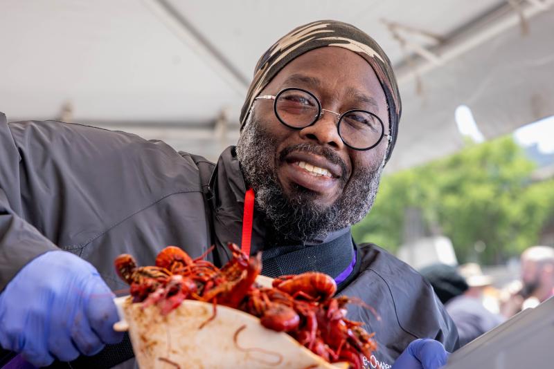 A man holds up scoop of crawfish and smiles for photo.