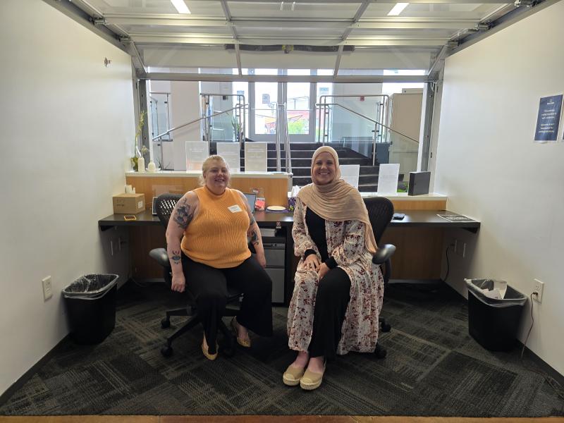two women smile for photo from reception desk