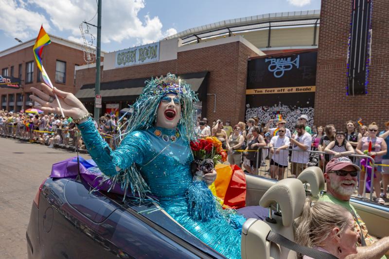 Drag queen participant waves from convertible in pride parade