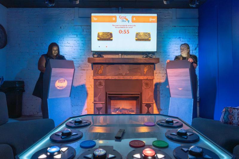 two people stand at game show stands in game nite lounge answering questions on screen