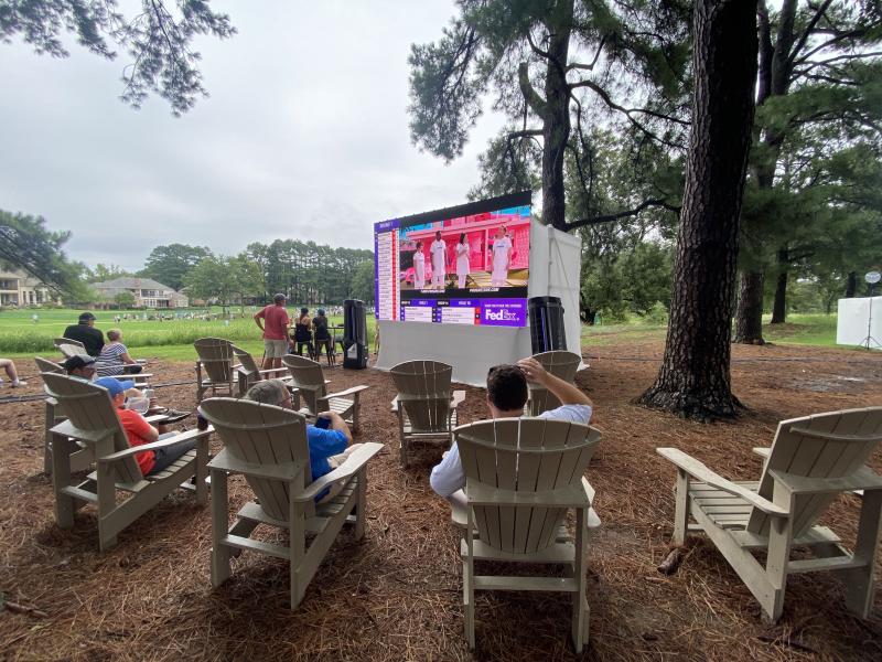 people in chairs surrounding tv screen playing golf tournament