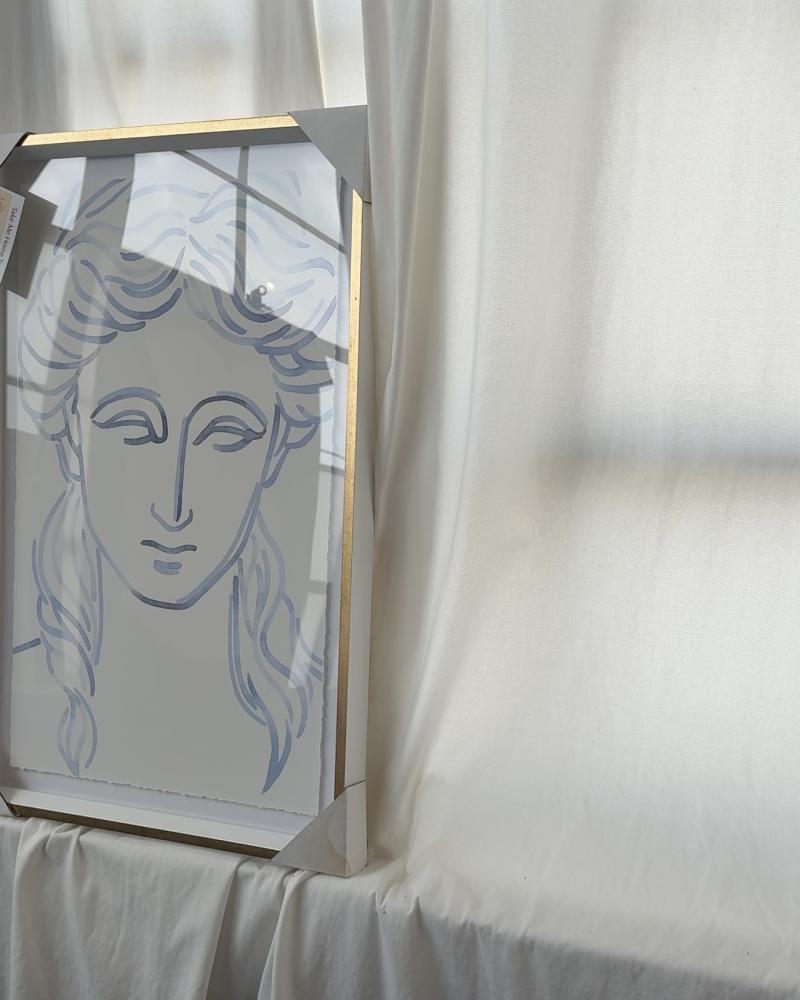framed art on white sheet backdrop. artwork is a sketch of a woman's face in blue