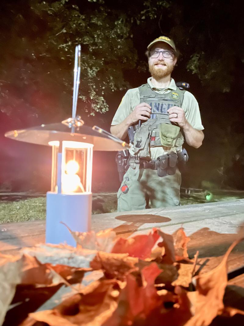 lit lantern on table, ranger smiles for photo behind
