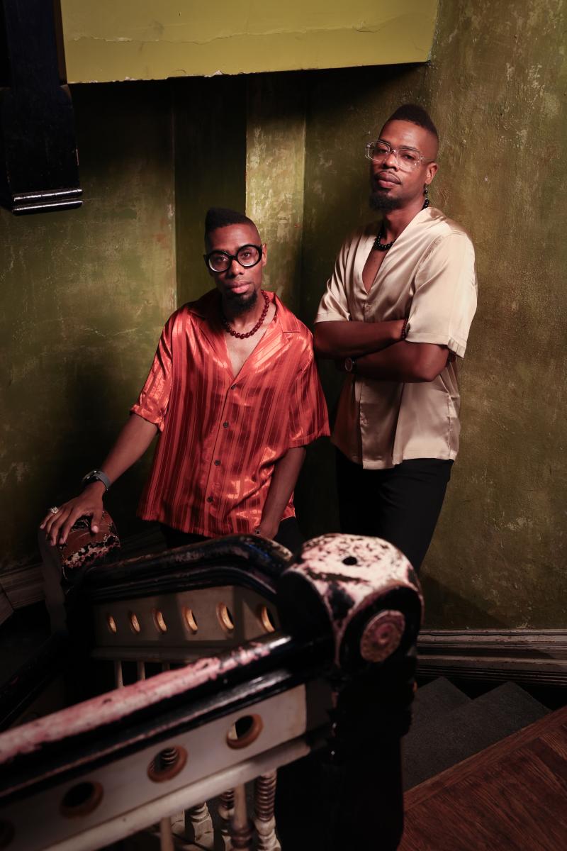 two african american men standing in a stair well with green background