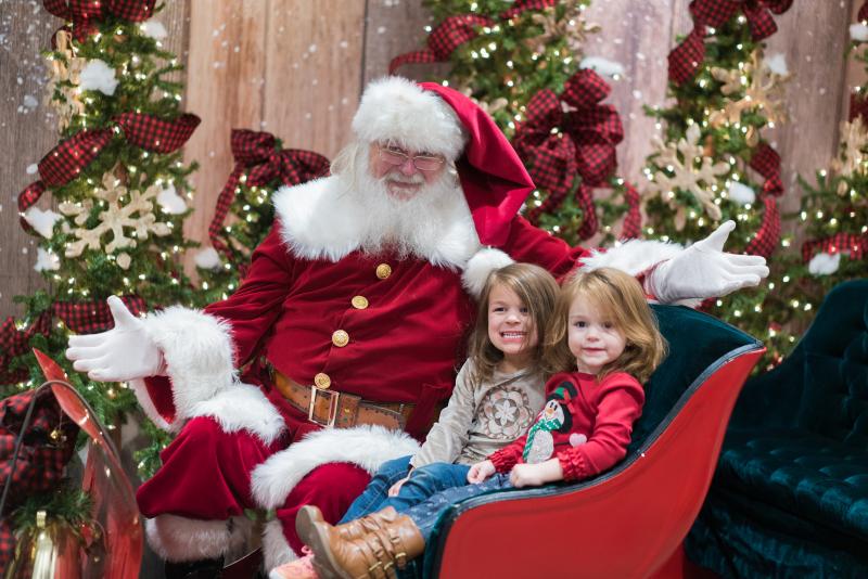 two children pose with santa for photo on sleigh
