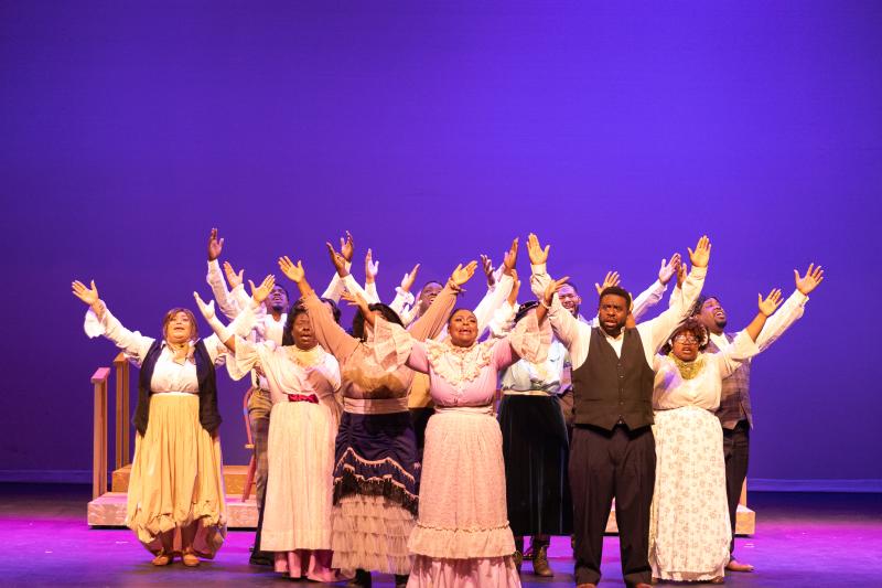 group of actors on stage with their arms raised right before they bow