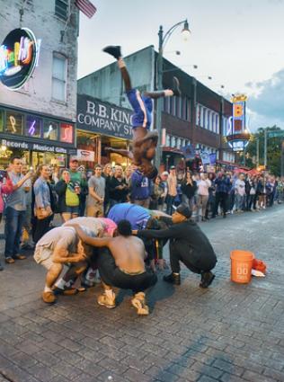 Beale Street Flipper flipping over a huddled group of people with a crowd watching on Beale Street.