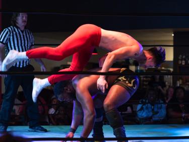 wrestler flies over the back of another wrestler who is bent over