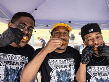 three men pose for photo eating hot wings