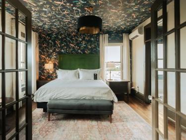 doors open into suite hotel room of Hotel Pontotoc with bed, wallpaper on back wall and ceiling