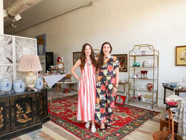 Two women standing next to each other surrounded by antiques