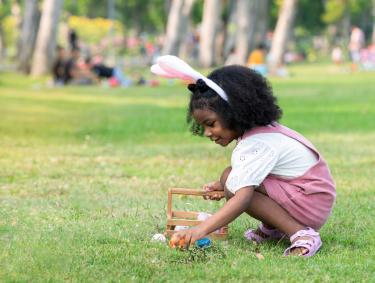 young girl finds egg in field during easter egg hunt