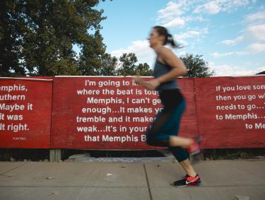 woman runs by memphis mural of music lyrics