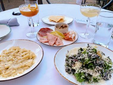 plates of pasta, salad, charcuterie, and cocktails on a white tablecloth on a patio