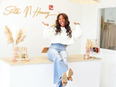 woman sitting on counter of brightly lit boutique, she's laughing and her hands are in the air
