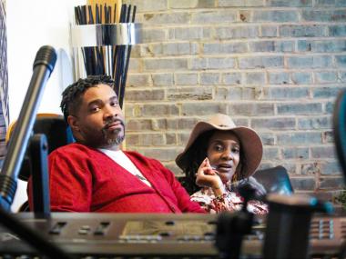 man in red jacket and woman in hat sitting in music studio