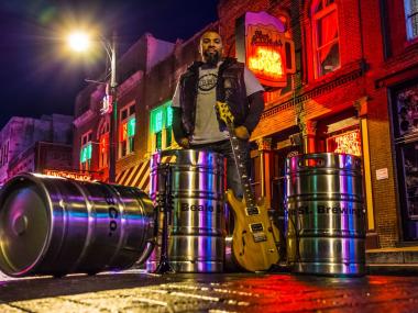 man standing behind several shiny silver kegs stacked up, Beale Street is visible in the Background
