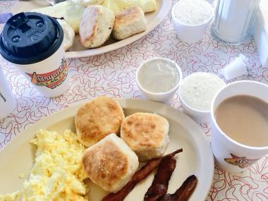 spread of breakfast food, including biscuits, eggs, bacon, and coffee