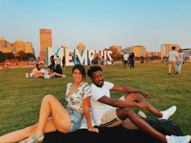 man and woman sitting in front of the MEMPHIS sign at mud island in a field