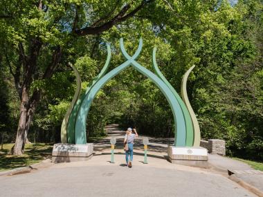 green sculptural gate entrance to old forest trail, woman walking through