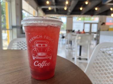 dark pink colored iced tea in a plastic cup in the foreground, background is coffee shop interior with white chairs and lots of windows