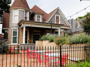 gray house with turrets that's been turned into a restaurant, shrubs all around, patio with red furniture out front