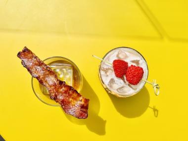cocktail with bacon and cocktail with raspberries sitting on a yellow table