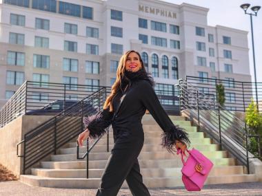 woman in black jumpsuit walking with pink purse in front of multi-story memphis hotel