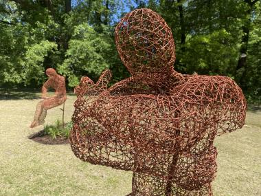 two metal wire silhouettes of a man with crossed arms and other looking down
