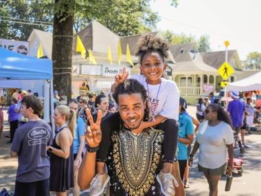 man with young girl on shoulders both hold up peace signs at Cooper young festival