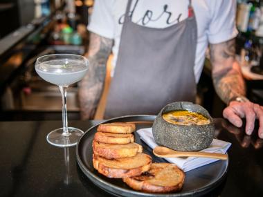 man stands behind bar with appetizer and mocktail sitting on bar
